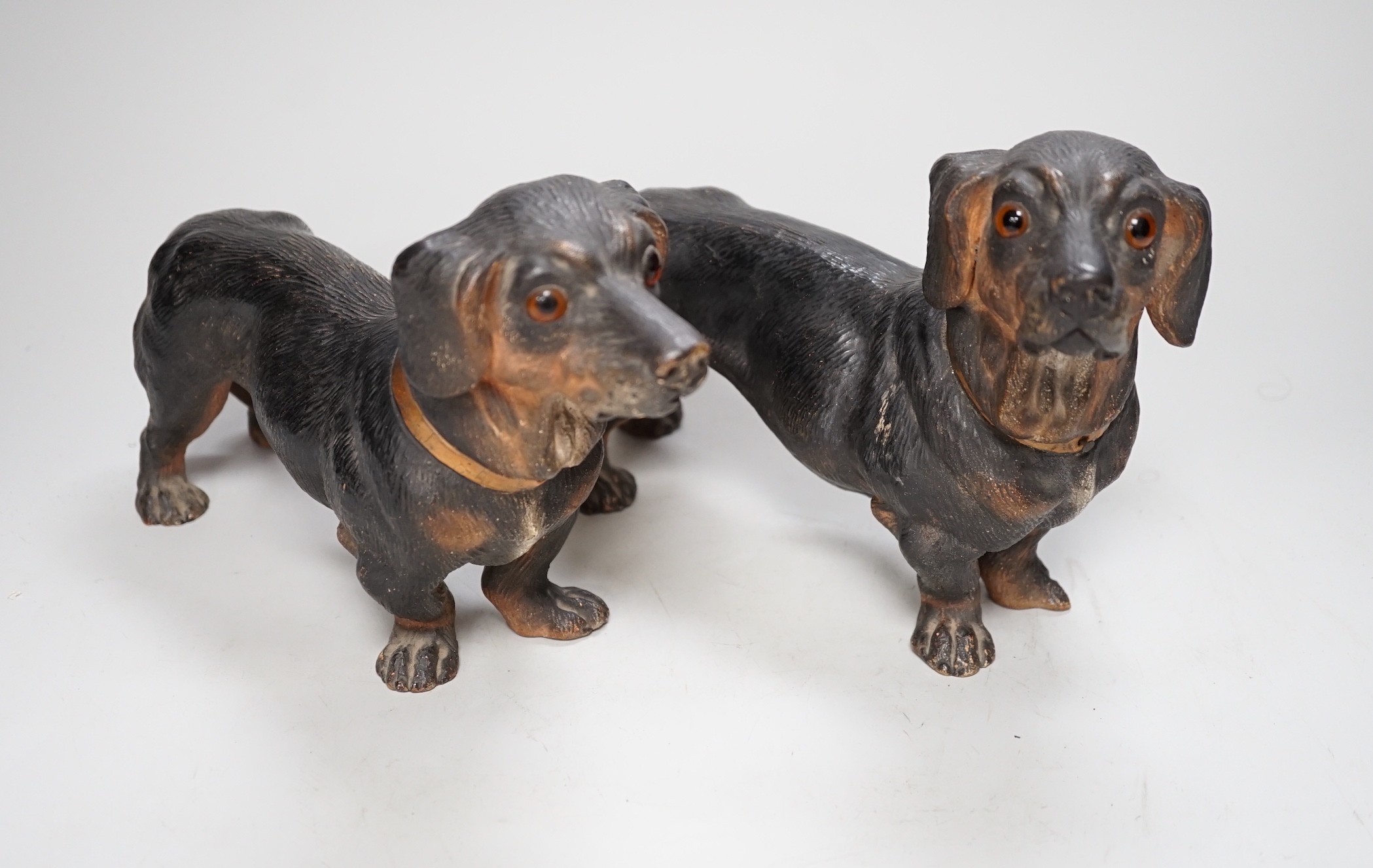 A pair of Austrian cold painted terracotta models of Dachshunds, one paw damaged, inset glass eyes 28cm long